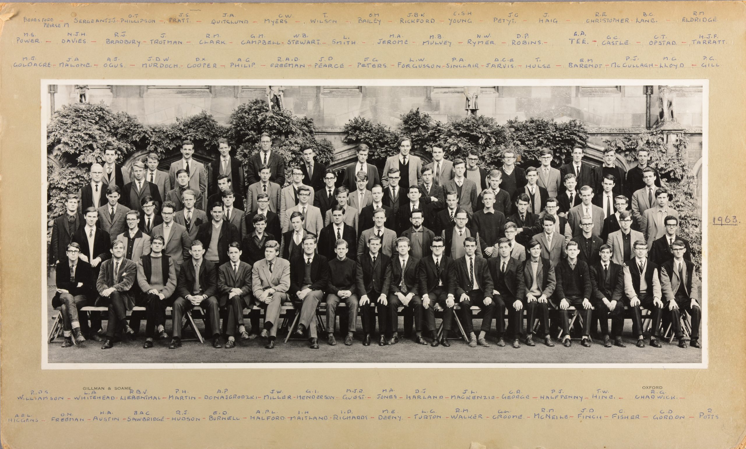 Black and white photograph of the students who matriculated in 1963. Around 80 men standing or sitting, in 5 rows, in the Cloisters. They are all smartly dressed; the majority in a suit and tie. On the frame of the photograph, the initials and surnames of the men are handwritten in blue ink.