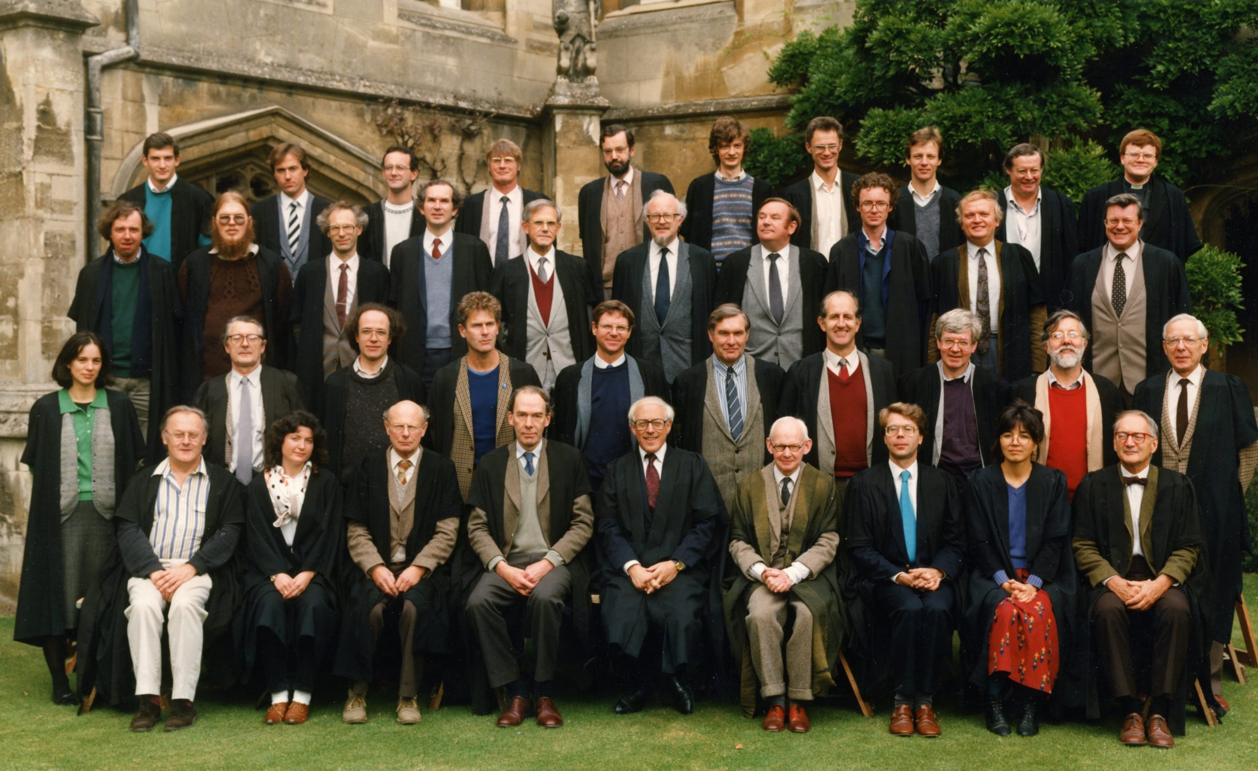 Colour photograph of around 40 Magdalen Fellows standing in 4 rows. They are all white men, with the exception of 3 women. One of the women is Beth Okamura.